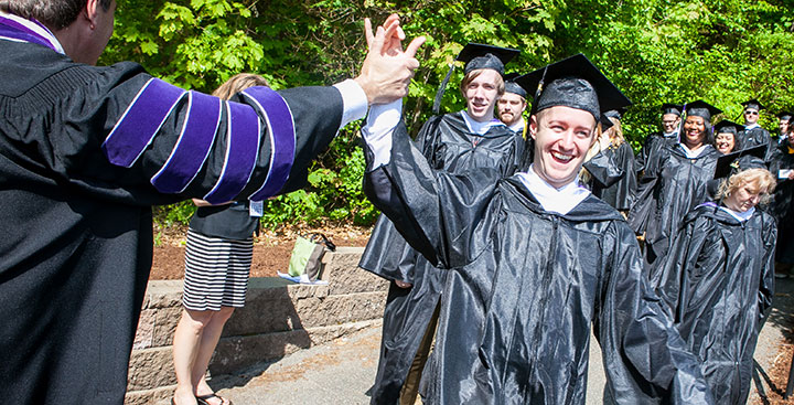 A Curry College graduate receives a high five from the College's President on Commencement Day