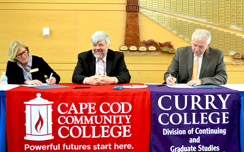 Curry College Provost Dr. David Szczerbacki signs transfer agreement as Dr. Susan Miller, and Dr. John Cox  from Cape Cod Communtiy College look on.