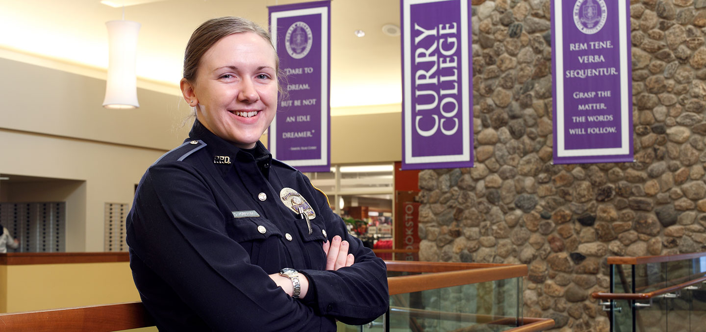 A Curry College Master of Arts in Criminal Justice Degree student in a police uniform smiles for a photo