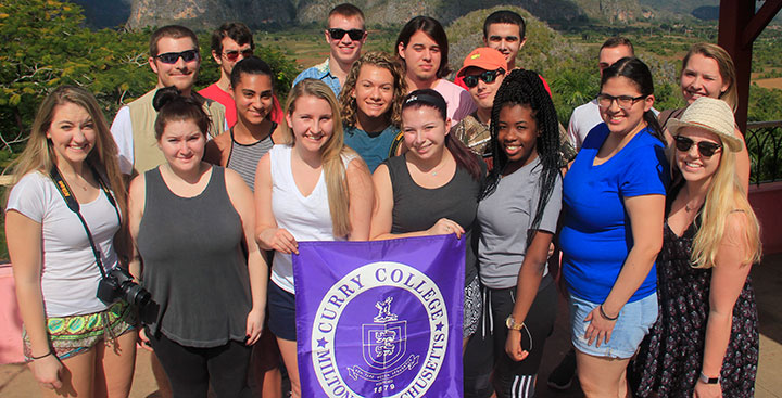 Students pose for a picture with a CurryCollege branded sign in Cuba