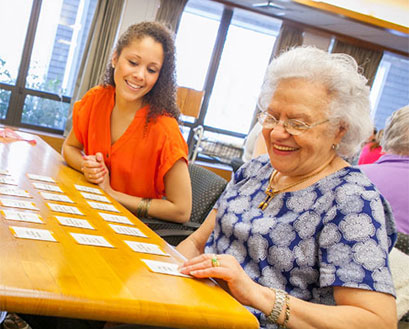 A Curry College nursing student plays cards with an elderly community member
