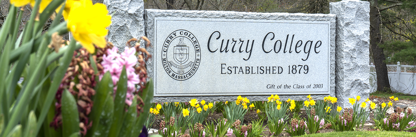 Curry College campus front gate sign and spring flowers