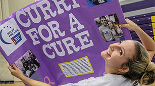 A student holds up a "Curry for a Cure" sign at the Involvement Fair