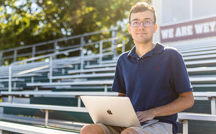 Jesse Cinquini writing on his computer at football field bleachers