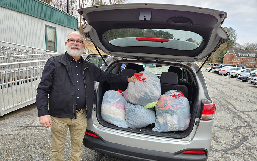Professor Jim Jabbour Proudly Stands Next to Clothing Bags for Donations