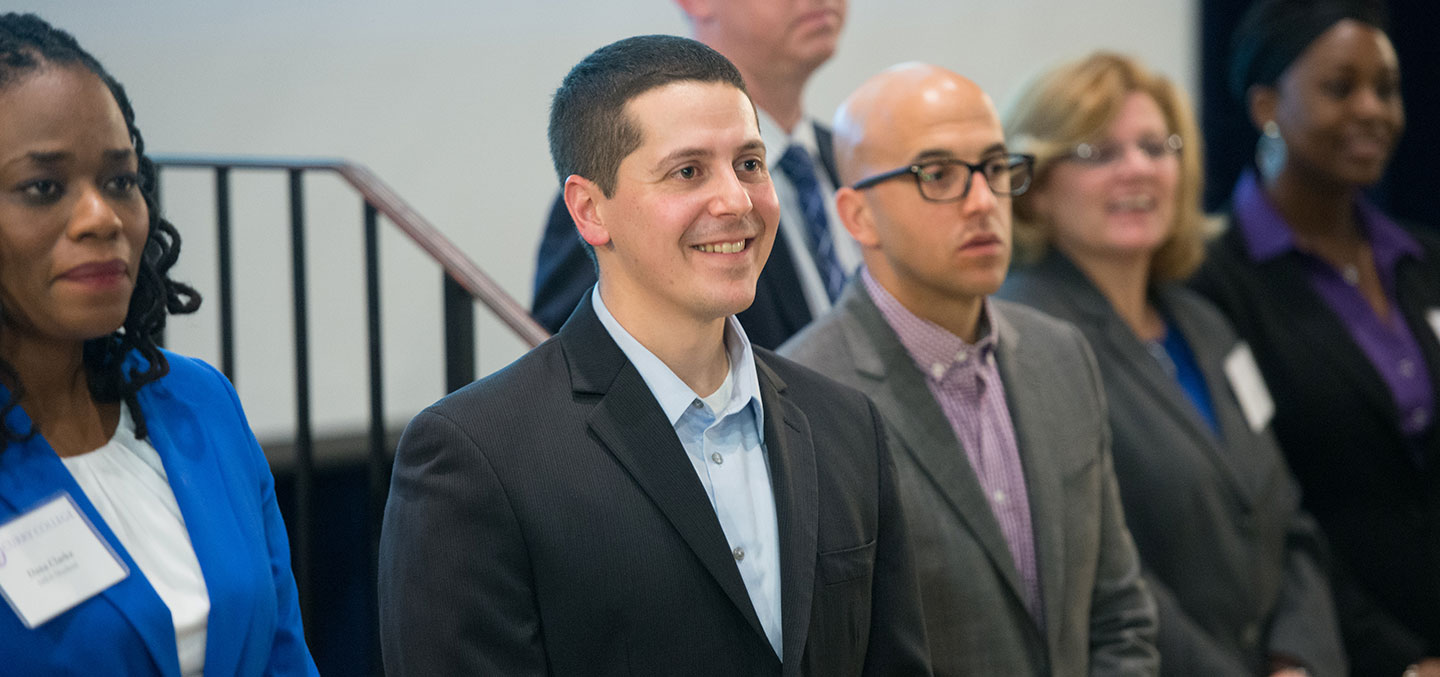 A Curry College MBA Degree student smiles and stands with his cohort after completing the Master's program