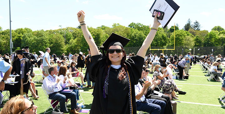 A Curry College graduate throws her hands in the air in celebration