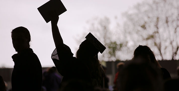 A student raises her diploma at Curry College Commencement