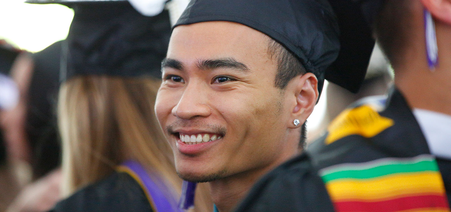 A student in cap and gown smiles proudly at Curry College Commencement