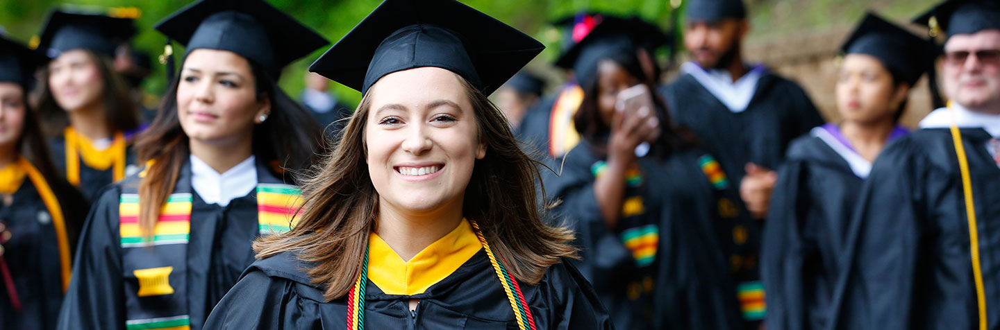 A student in cap and gown smiles proudly at Curry College Commencement