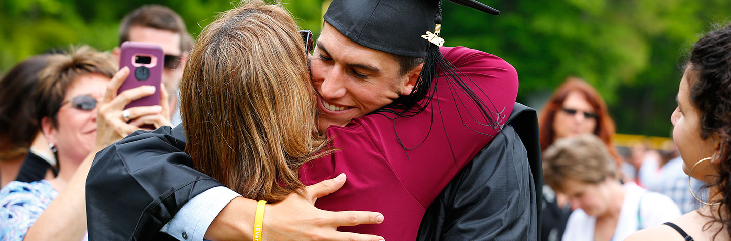 A student in cap and gown hugs his mother at Curry College Commencement