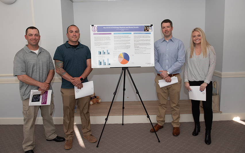 Four MACJ students post next to Capstone project poster