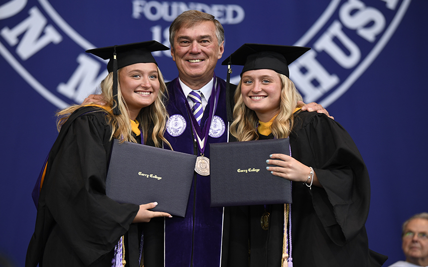 President Quigley poses with twin sister graduates at the 2023 Commencement