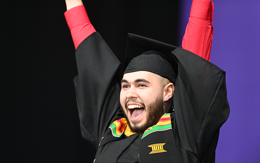 student raises arms as they cross the commencement stage