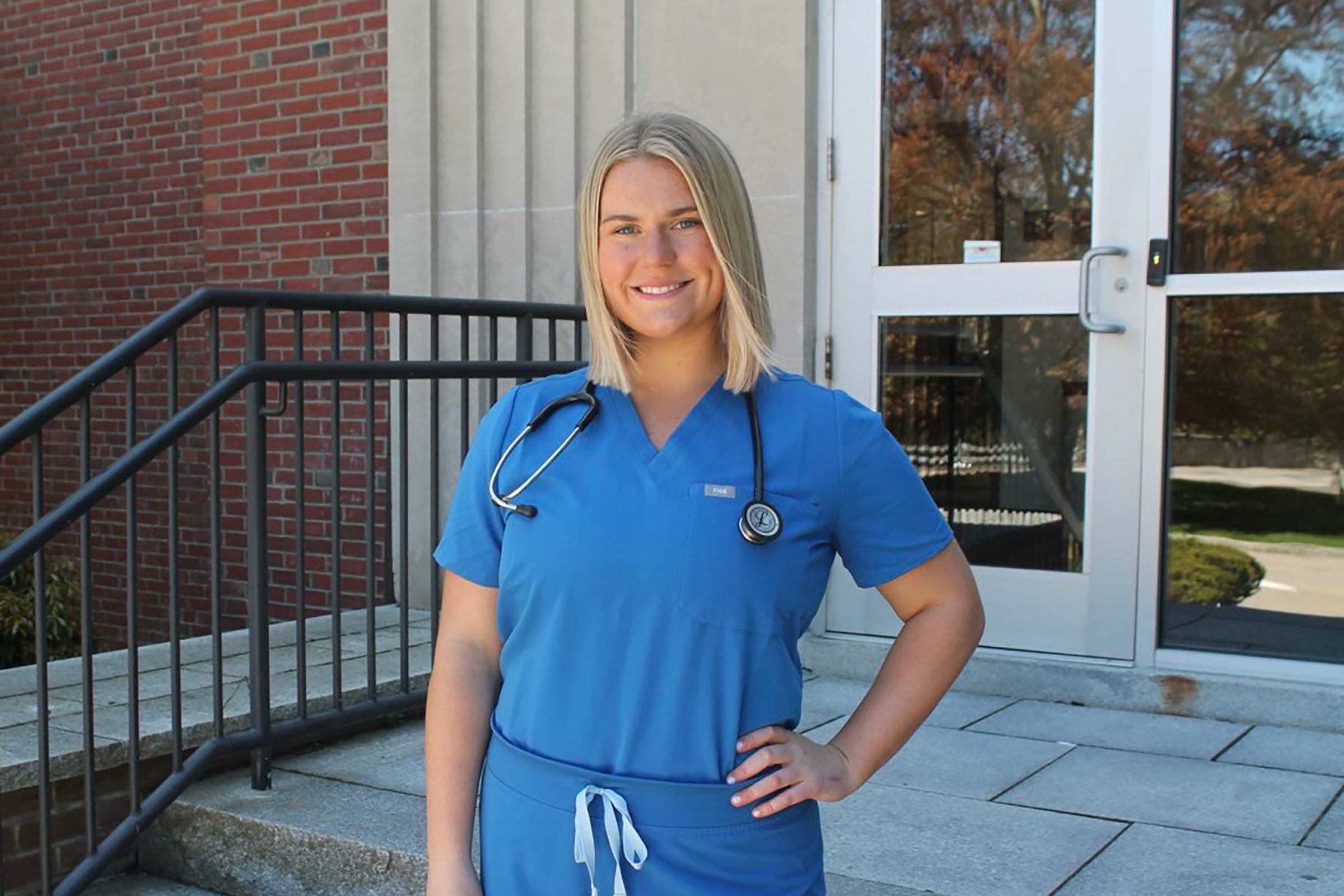 Ellie poses outside Nursing building in blue scrubs
