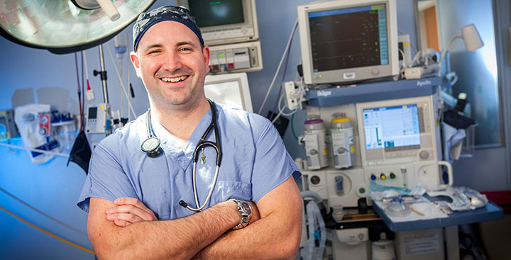 A Curry College nursing alumnus stands in a hospital emergency room in scrubs