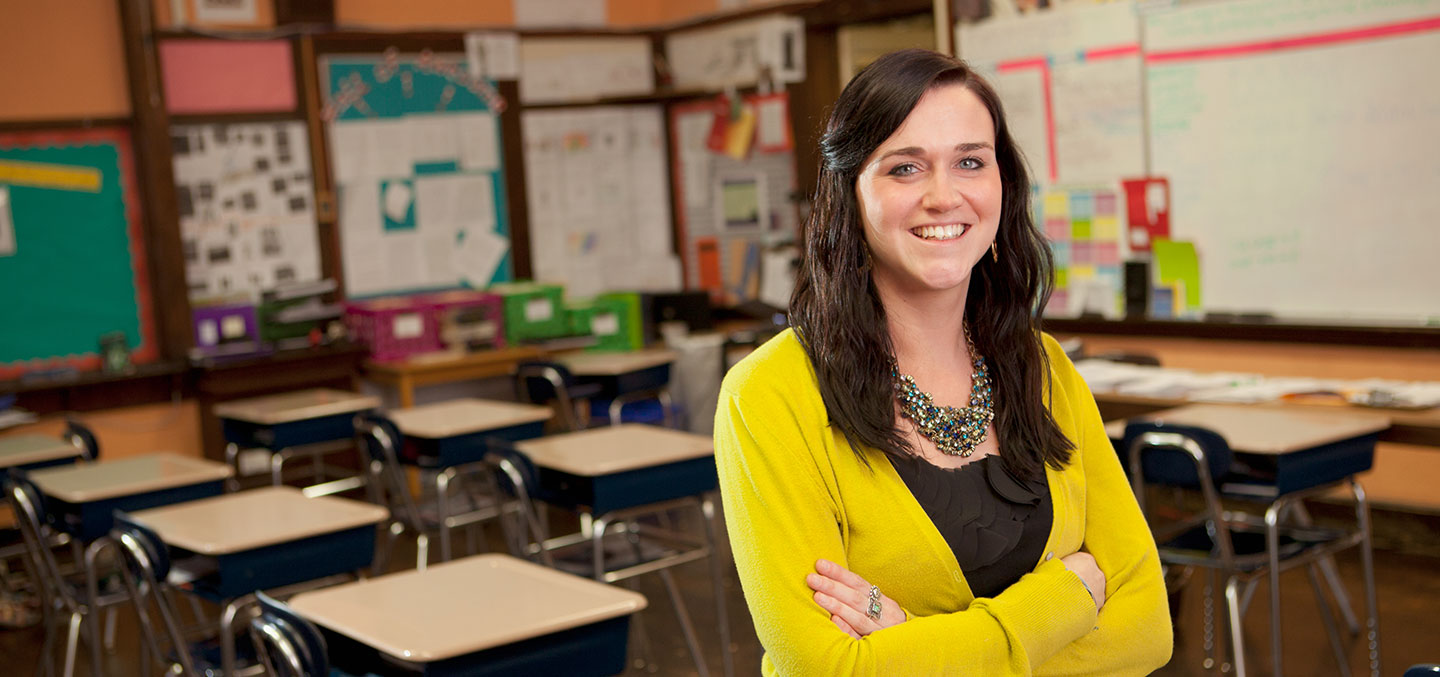 A Curry College Master of Education (M.Ed.) Degree student smiles and stands in her own classroom after completing the Master's program