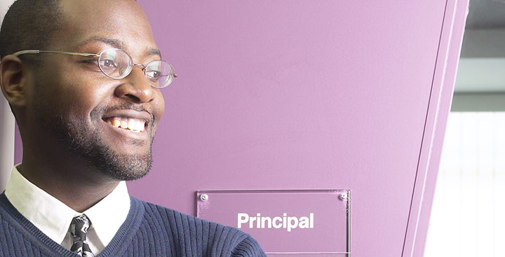 A principal stands outside his office representing the Curry College PSL Certificate program