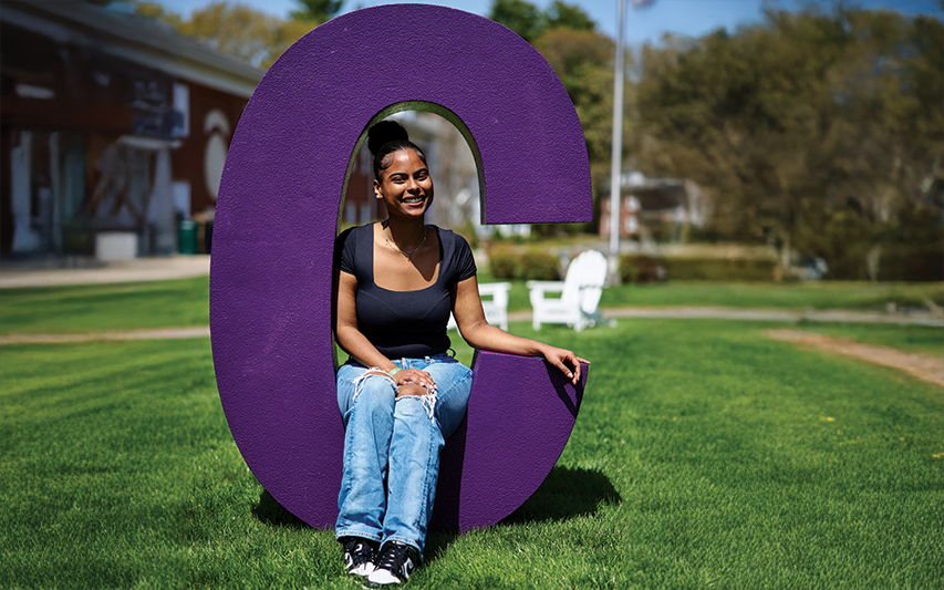 A Curry student sits in the middle of a purple "C" on the Quad