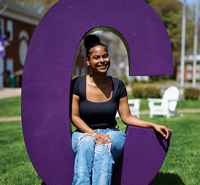 A student sits in a big purple letter 'C'