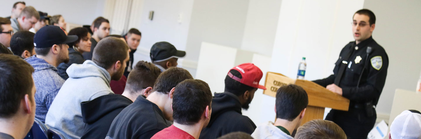 Students pursuing a Criminal Justice Degree or Sociology Degree at Curry College listen to an officer speak in class