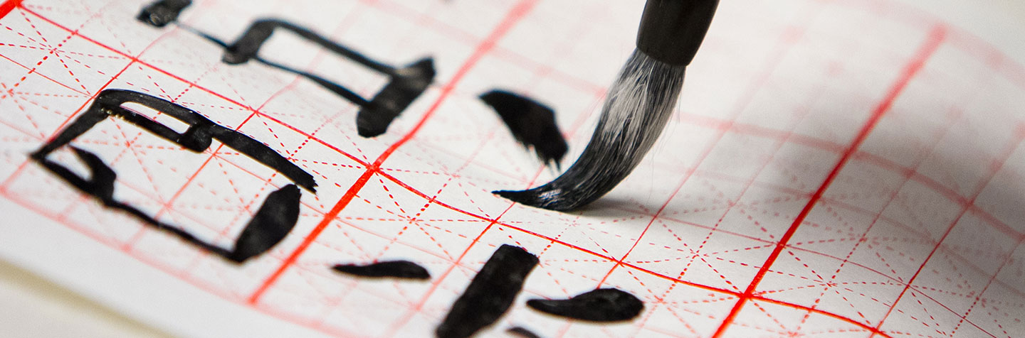 Student in the Foreign Languages Program at Curry College writes in Chinese on a scroll