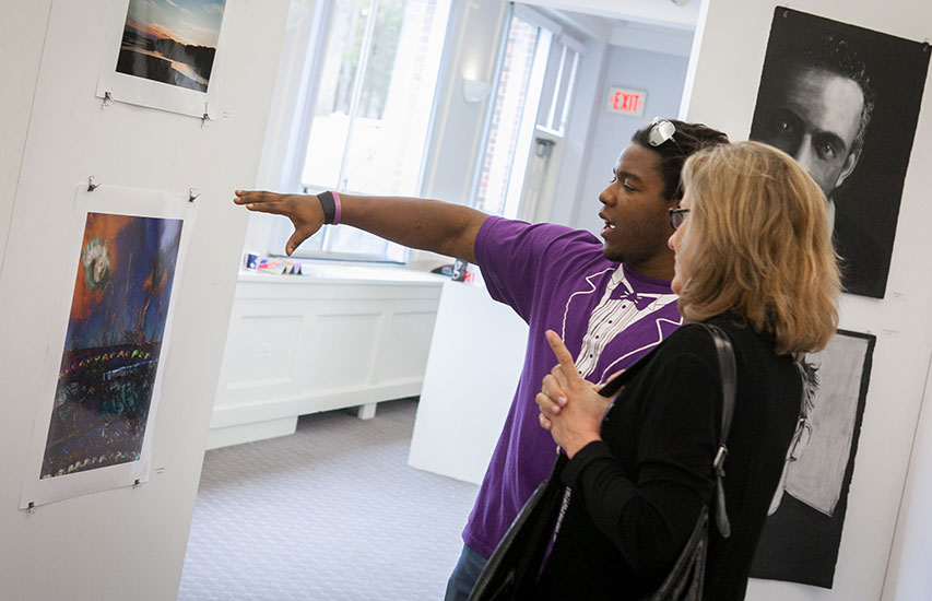 Student showcasing his work at a campus art exhibit representing the Art History minor at Curry College