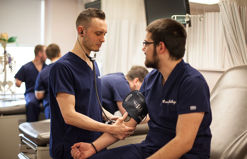 Two students perform duties in a lab setting while persuing a Nursing degree at Curry College