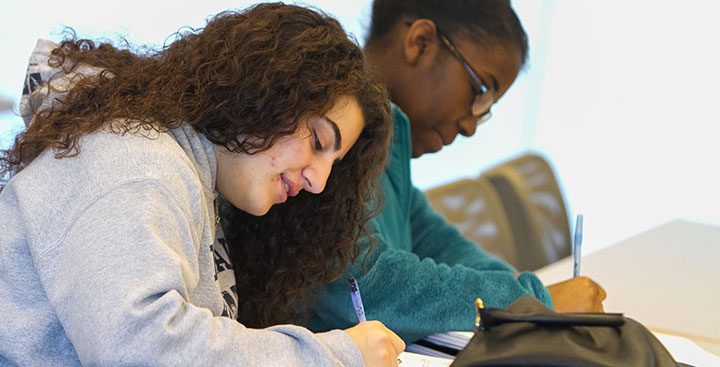 Two writing students take notes in class