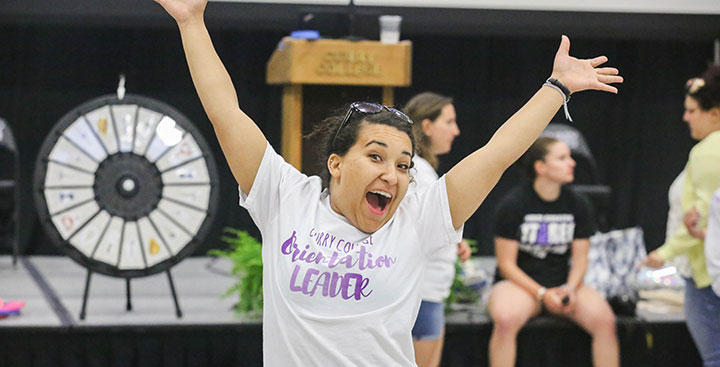 A student with her arms in the air cheering at Orientation