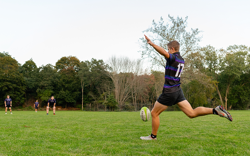 Curry Colege Rugby player kicks a ball to his teammates