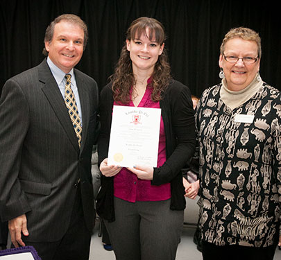 Alumna poses with certificate and faculty members