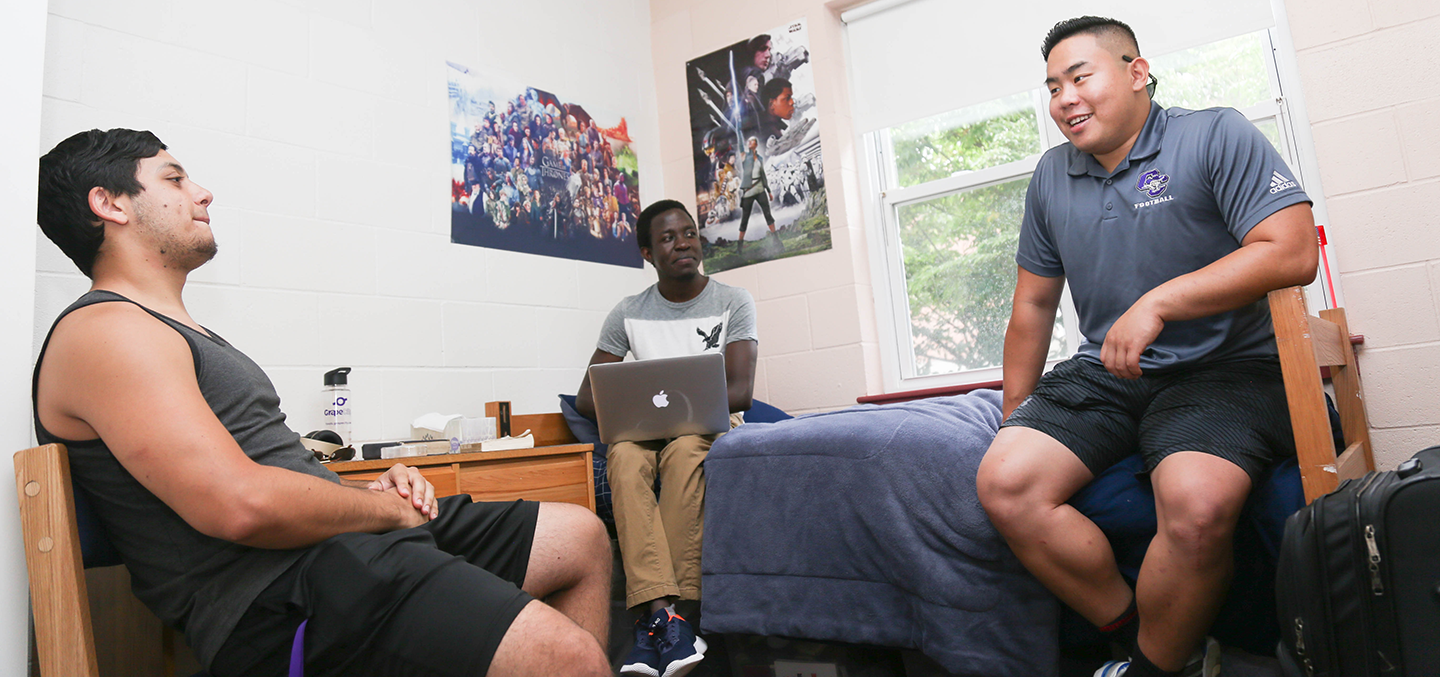 Three male students hanging out in a residence hall room