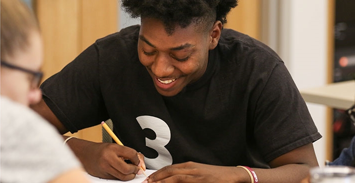 A Curry College students smiles while doing a First-Year class assignment