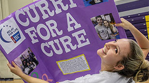 A student holds up a "Curry for a Cure" sign at the Involvement Fair