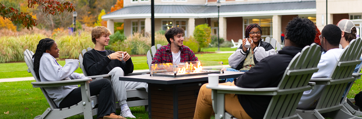 Curry students chat around a fire in autumn on campus