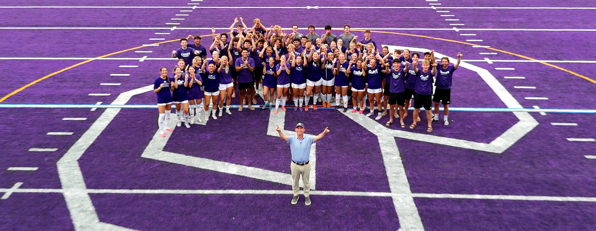 Curry College President Jay Gonzalez with student-athletes on the newly purple Katz Field